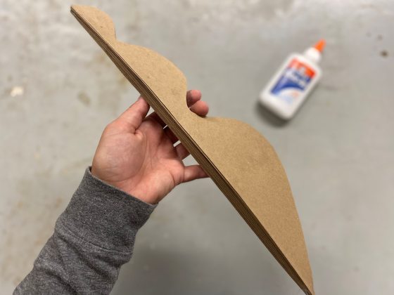 A person holding brown paper cutouts in the shape of a long ornament.